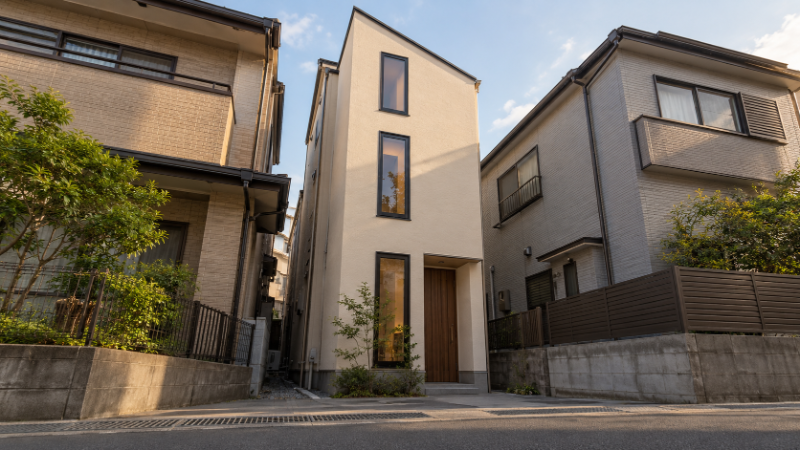 都市部の狭い敷地に建つ細長い3階建ての木造住宅を道路の反対側から見上げた外観