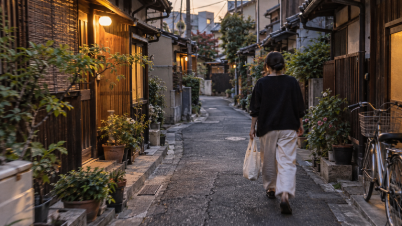 下町の路地を買い物袋を提げて歩く人の後ろ姿(イメージ・AI生成)