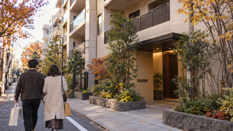 東京の住宅街の中層マンションと、歩道を歩く夫婦の後ろ姿