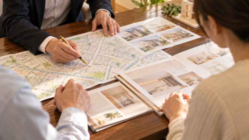 相談室で担当者が夫婦に住宅街の地図と資料を示して説明している手元